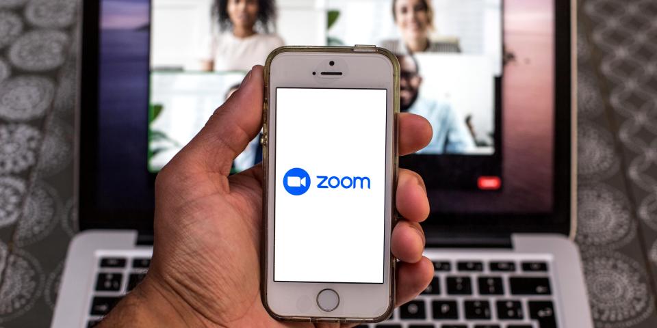 Zoom app seen displayed on a smartphone screen and a Zoom Desktop on a laptop in the background.