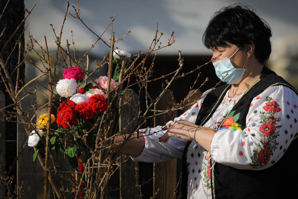 A woman wearing a face mask places knitted flowers in a bush during a spring charms fair at the Dimitrie Gusti Village Museum Museum in Bucharest, Romania, Feb. 27, 2021. Millions of East Europeans celebrate the arrival of spring on March 1 with charms tied with red-and-white string, a centuries-old custom symbolizing hope and a new season. (AP Photo/Vadim Ghirda)