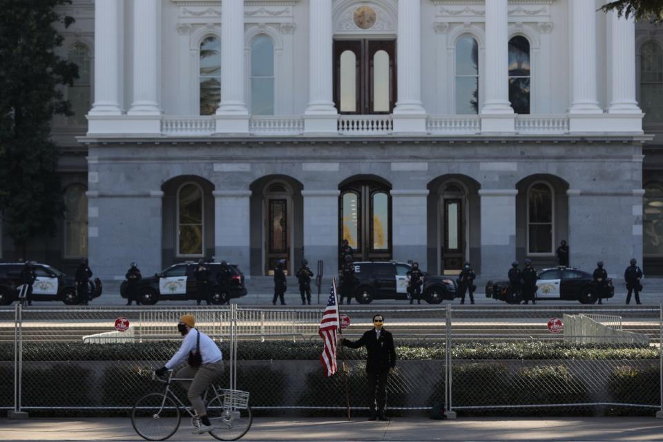 UCR masters student Christian Alvarado, 25, stands with an American flag in front of capitol.