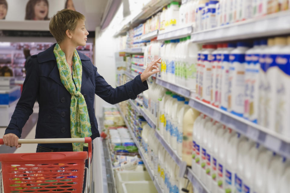 Person shopping, choosing products off grocery store shelf with basket in hand