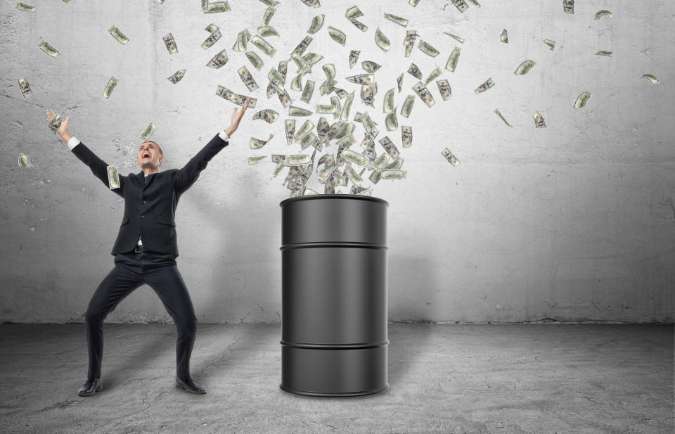 An oil barrel with money spewing out of it with a happy man celebrating next to it.