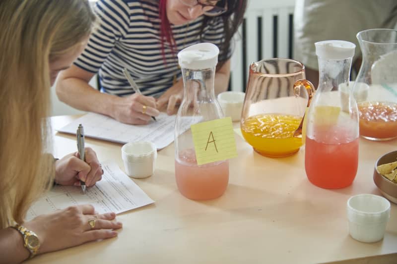 candid photo of Apartment Therapy/The Kitchn staff taste testing multiple different margarita mix flavors from pitchers and jotting down their opinions