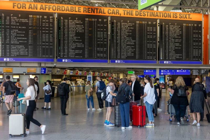 Travelers stand in front of a display board in the terminal at Frankfurt Airport, where numerous departures have been cancelled. Climate activists had forced their way onto the airport premises early in the morning and stuck to the board. Helmut Fricke/dpa