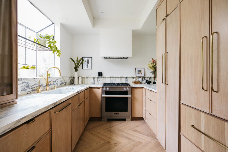 A kitchen with light wooden cabinetry, herringbone flooring, and marble countertops