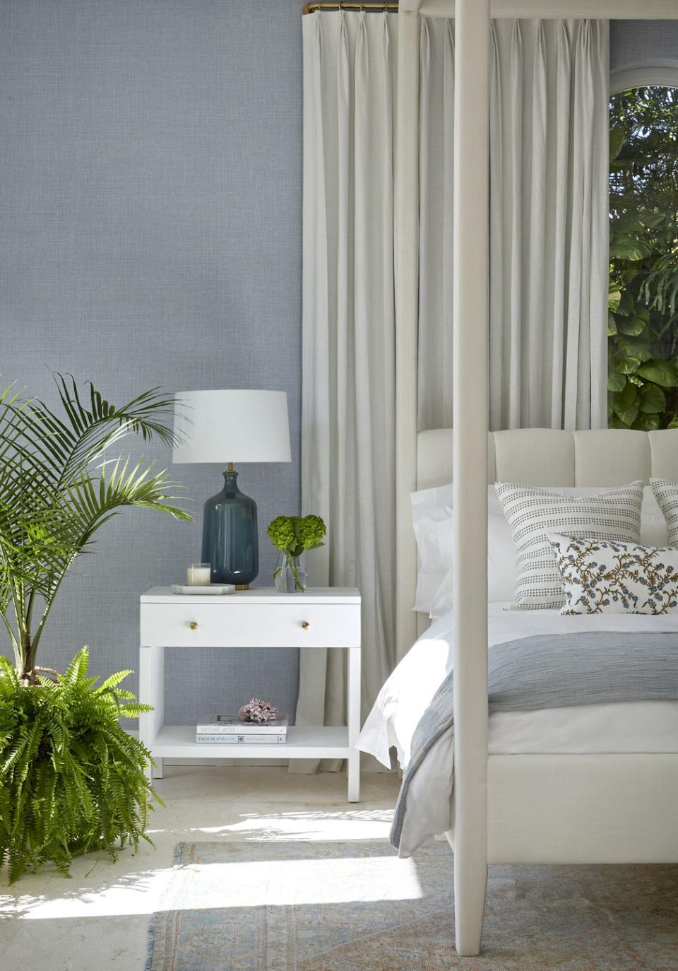 a white bed with a white lamp and a white table with a plant