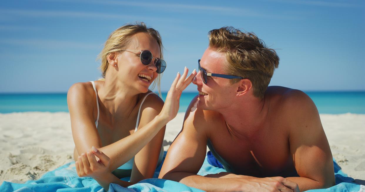 A happy young couple is having fun to apply a sunscreen or sun tanning lotion to take care of their skin during a vacation on a beach. - Credit: HQUALITY - stock.adobe.com