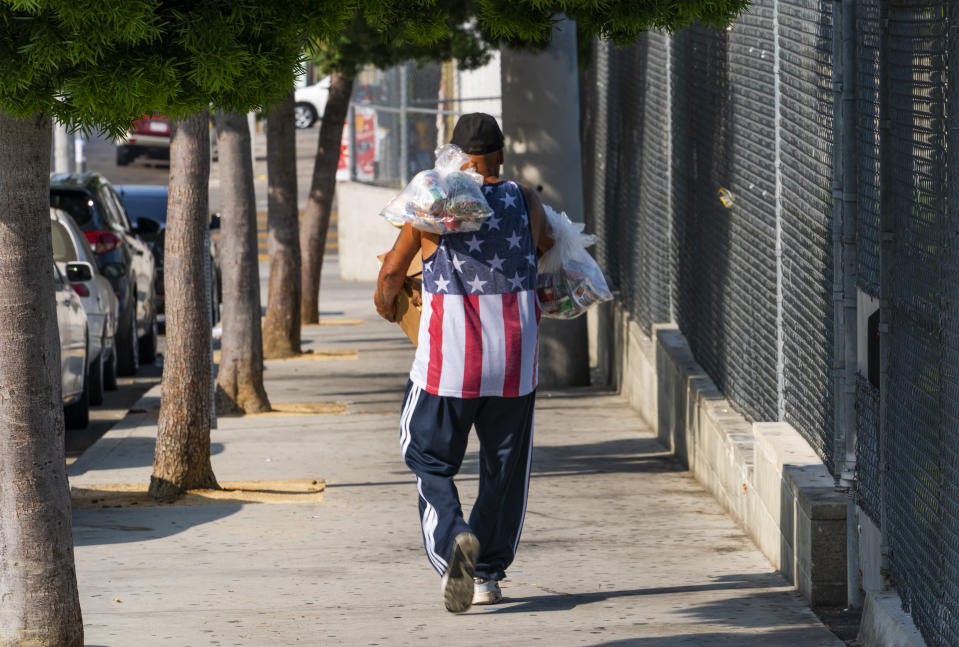 Parent Ernesto Cortes walks away with his children's free school lunches and a weekend box, after picking them up on Friday, July 16, 2021, at the Los Angeles Unified School District's Liechty Middle School in Los Angeles. Flush with cash from an unexpected budget surplus, California is launching the nation's largest statewide universal free lunch program. When classrooms open for the fall term, every one of California's 6.2 million public school students will have the option to eat school meals for free, regardless of their family's income. (AP Photo/Damian Dovarganes)