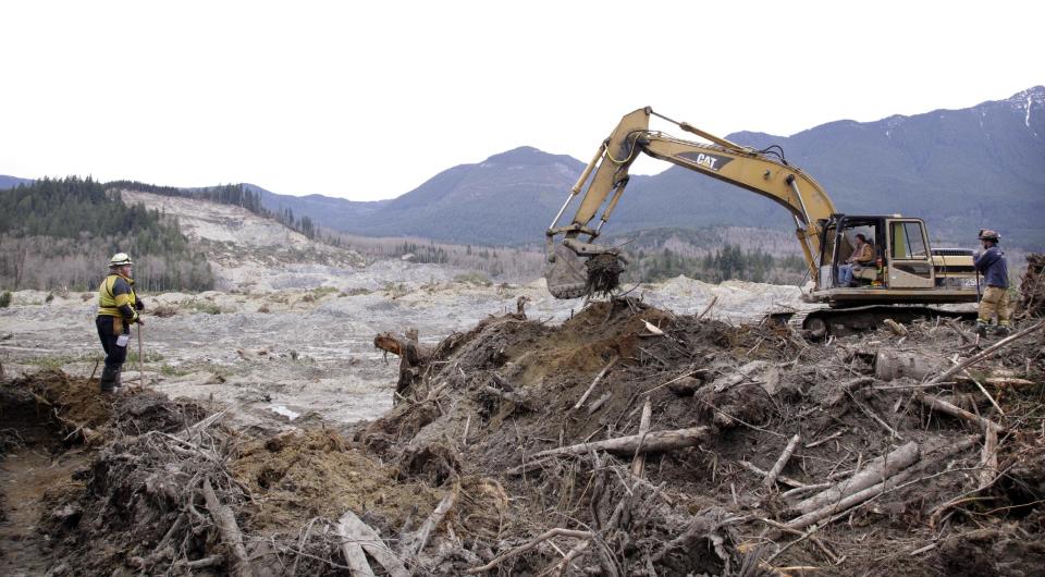 Workers move debris at the scene of a deadly mudslide, torn off from the hill at upper left almost two weeks earlier, Thursday, April 3, 2014, in Oso, Wash. More than a dozen people are listed as missing and 30 bodies have been found in debris from the March 22 landslide that broke off a steep hill, roared across the North Fork of the Stillaguamish River and buried a community at Oso, about 55 miles north of Seattle. (AP Photo/Elaine Thompson)