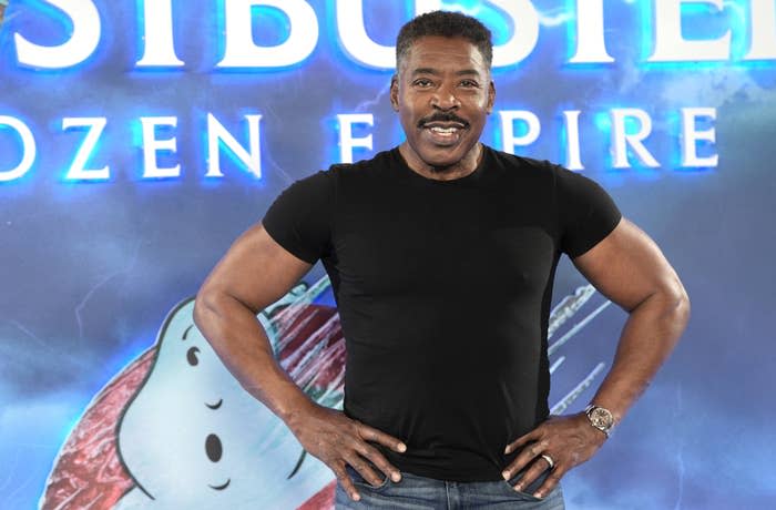 Ernie Hudson wearing a black shirt, posing in front of a "Ghostbusters: Afterlife" backdrop with character art