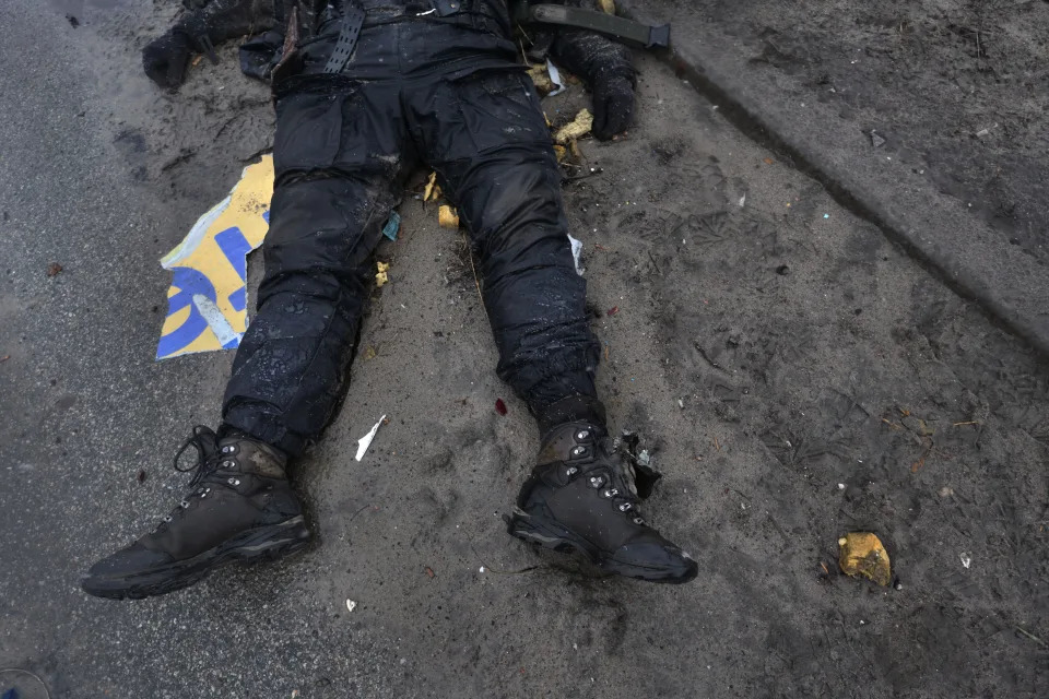 A body of a person wearing black clothing and boots lies in the street in Bucha. 