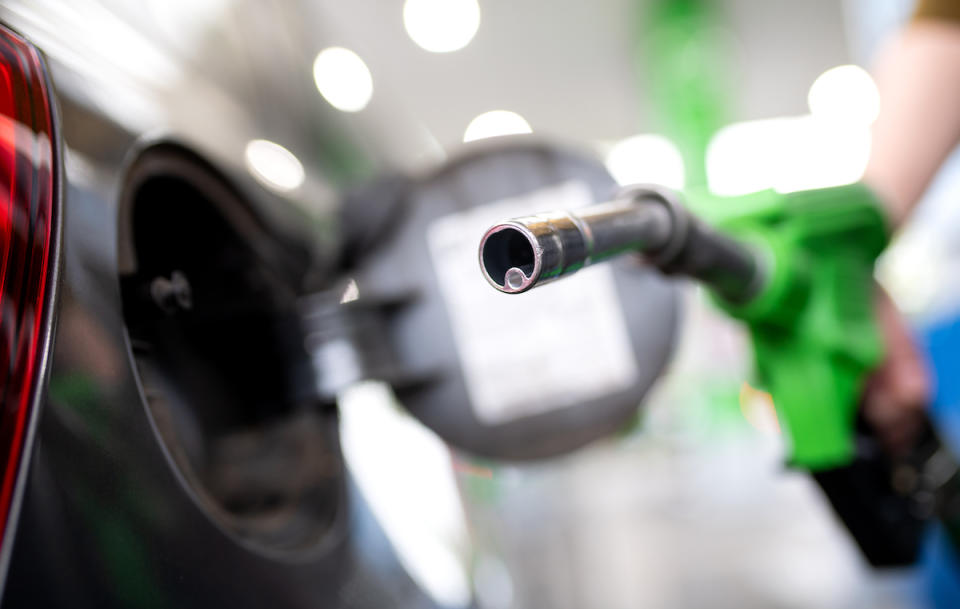 Eine Frau hält an einer Tankstelle eine Zapfpistole in der Hand und betankt ein Auto.