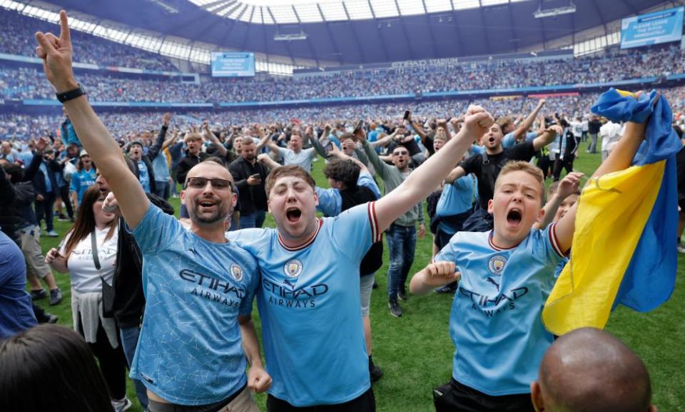 Manchester City fans celebrate on the pitch after the final whistle.