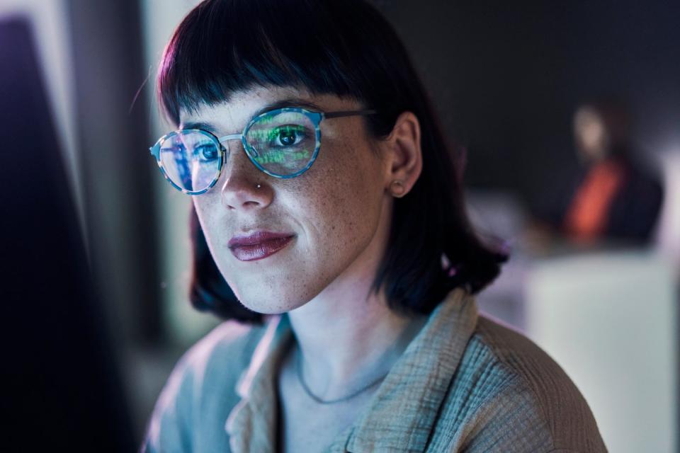 A business person looking at charts on a computer with light reflecting off their glasses.