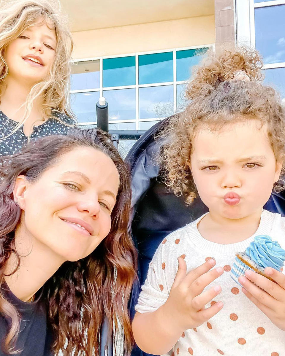 Tammin Sursok poses with her two daughters, Phoenix and Lennon. Phoenix is wearing a black dress with white polka dots, Tammin wearing a black top, and Lennon is wearing a white top with red polka dots and her curly hair tied up.