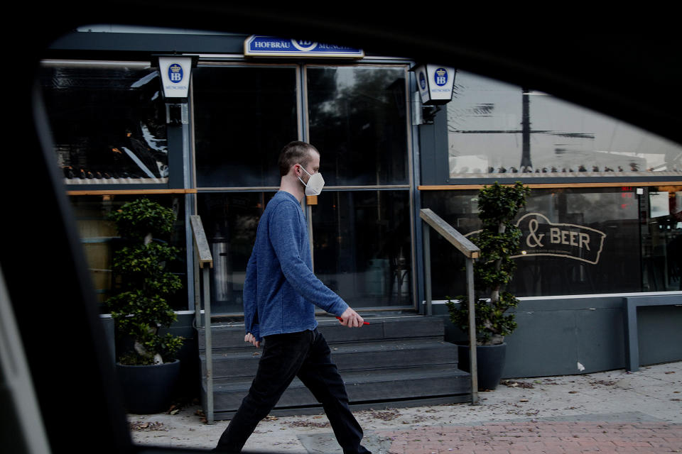 A man wearing in a mask is seen through a window car as he walks outside of a closed pub in central Nicosia, Cyprus, on Tuesday, April 28 2020. Medical experts say the low number of new coronavirus infections is paving the way to start gradually lifting a strict day-at-home order that includes a night time curfew. (AP Photo/Petros Karadjias)