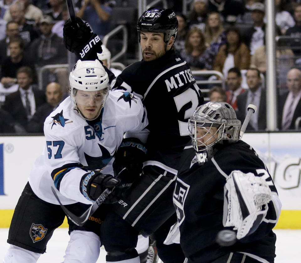 Los Angeles Kings goalie Jonathan Quick, right, blocks a shot by San Jose Sharks right wing Adam Burish, left, as Willie Mitchell looks on during the first period in Game 4 of an NHL hockey first-round playoff series in Los Angeles, Thursday, April 24, 2014. (AP Photo/Chris Carlson)