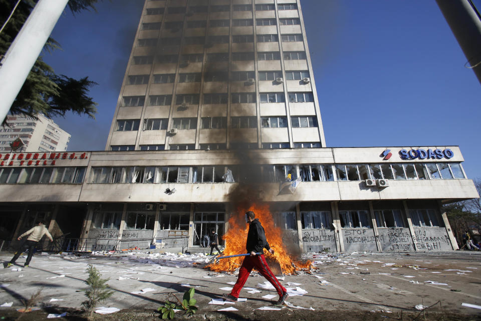 FILE - In this Friday, Feb. 7, 2014 file photo, a Bosnian protester walks past a local government building during protests in Tuzla, Bosnia. The violence engulfing Bosnia in recent days, with scenes of burning government buildings and protesters pelting police with stones, has many root causes. One of them is the failed privatizations of state-owned companies. (AP Photo/Amel Emric, File)