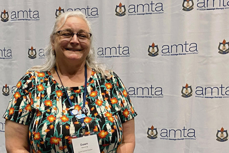 Dawn Menning, 55, of Aberdeen, S.D., poses at the American Massage Therapist Association national convention at the Huntington Convention Center in Cleveland, Ohio, Wednesday, Aug. 24, 2022. Menning said she wears scrubs to help drive home the professional and therapeutic nature of massage. Menning also keeps a large wooden spoon nearby in case someone tries something inappropriate. (AP Photo/Teresa Walker)