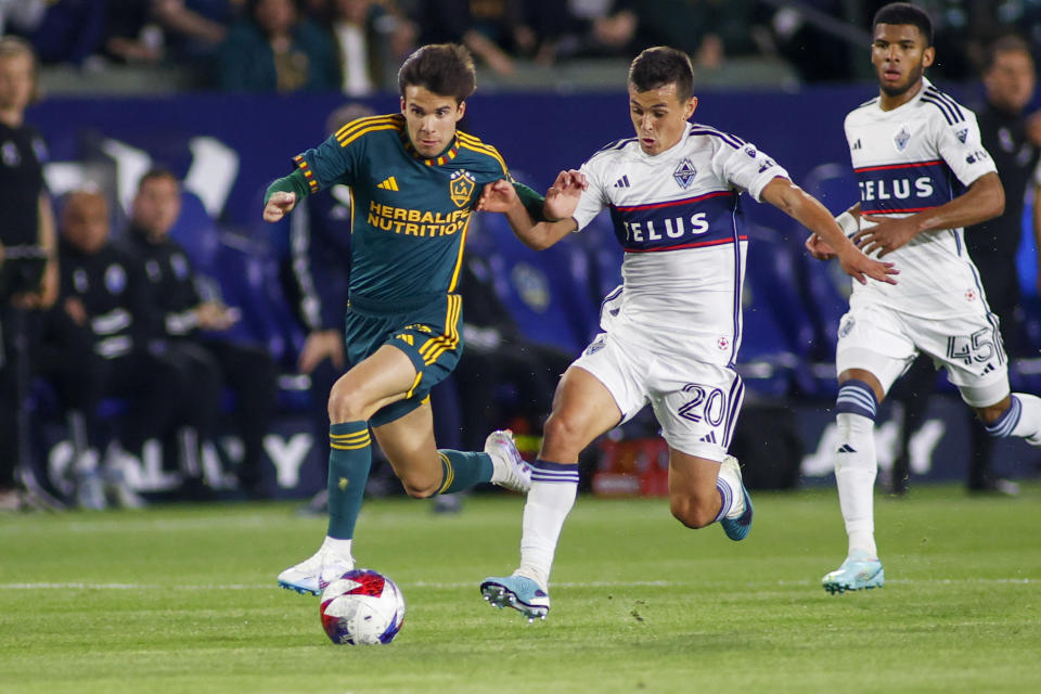 LA Galaxy midfielder Riqui Puig, left, and Vancouver Whitecaps midfielder Andrés Cubas chase the ball during the second half of an MLS soccer match in Carson, Calif., Saturday, March 18, 2023. (AP Photo/Ringo H.W. Chiu)