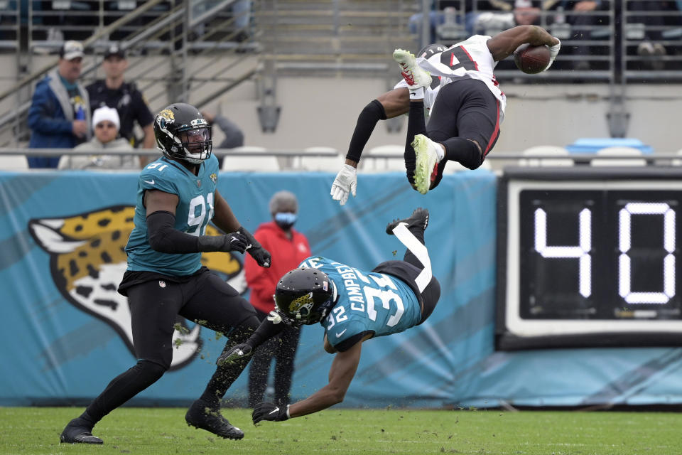 Atlanta Falcons wide receiver Russell Gage, top right, leaps over Jacksonville Jaguars cornerback Tyson Campbell (32) and defensive end Dawuane Smoot, left, after a reception during the first half of an NFL football game, Sunday, Nov. 28, 2021, in Jacksonville, Fla. (AP Photo/Phelan M. Ebenhack)