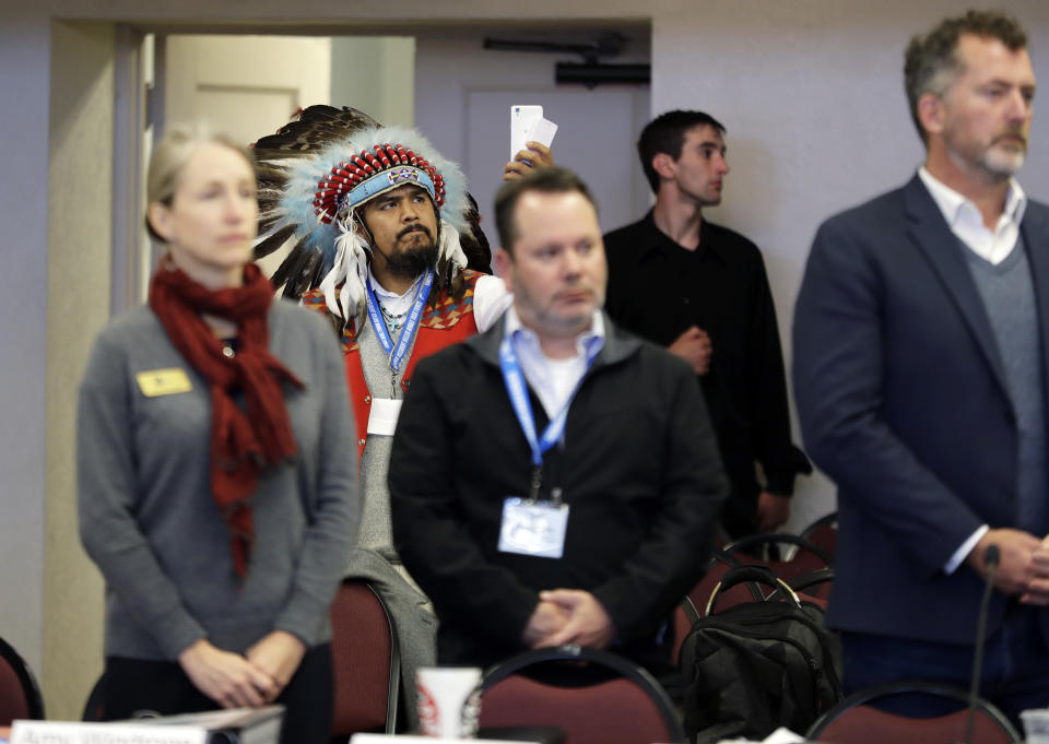 In this Oct. 17, 2018 photo, Jesse Nightwalker, second from left, of Tacoma, Wash., a member of the Palouse tribe, wears a ceremonial headdress as he takes video during a meeting of the Southern Resident Killer Whale Recovery Task Force in Tacoma. Nightwalker said he is in support of calls to breach four hydroelectric dams in Washington state as the plight of the critically endangered Northwest orca whales has captured global attention. (AP Photo/Ted S. Warren)