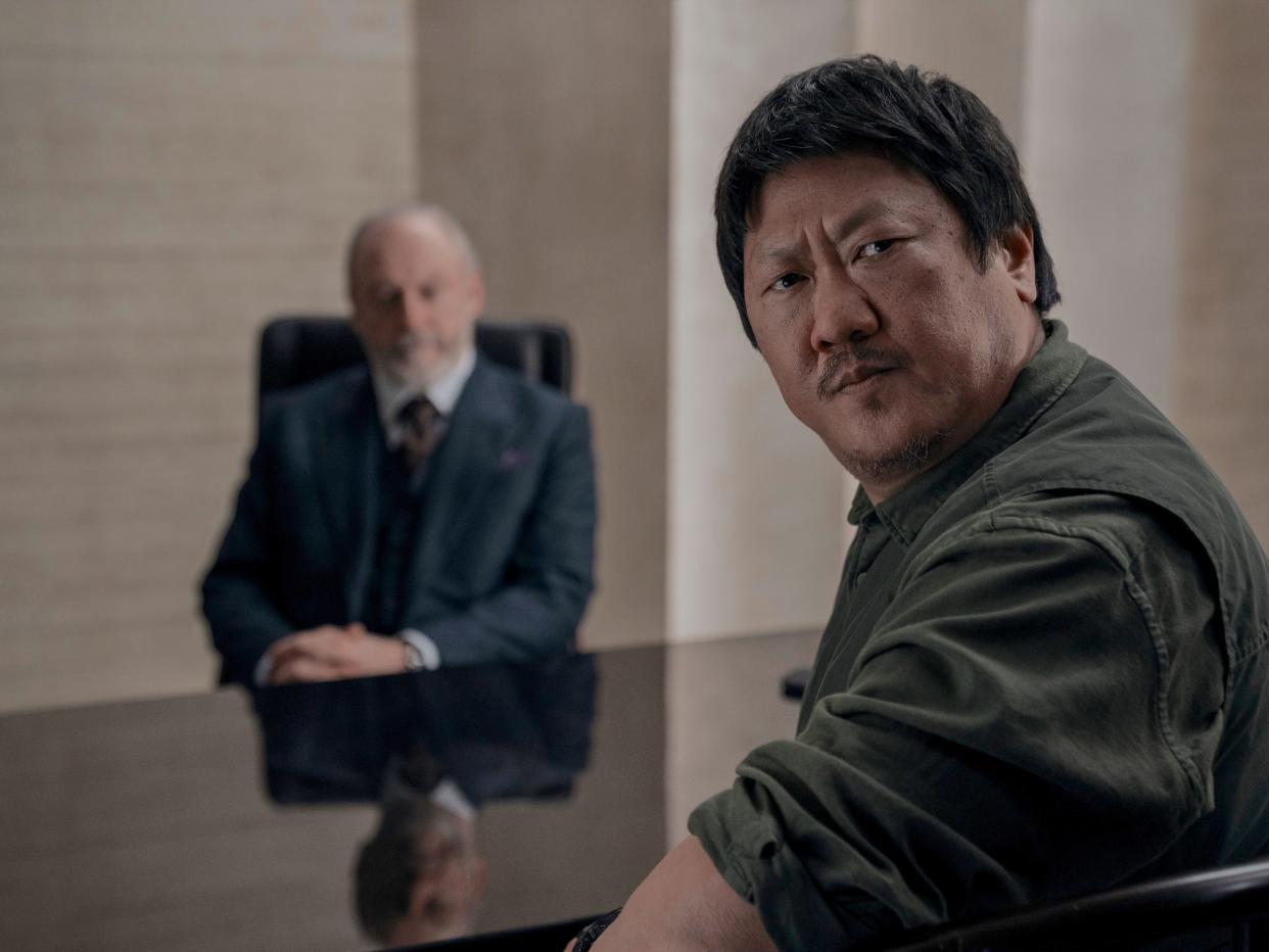benedict wong in 3 body problem, turning around in a chair to look backwards. liam cunningham is visible, blurry, in the background