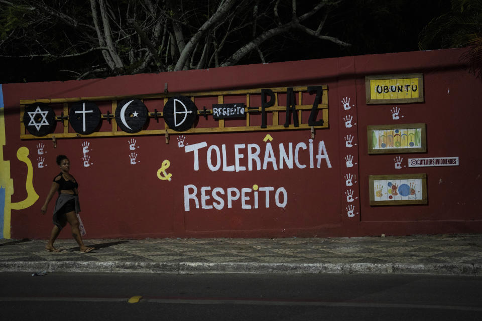 A resident walks past a school adorned with religious symbols representing Judaism, from left, Christianity, Islam and the Afro Brazilian faith Candomble, paired with the Portuguese words for peace, tolerance and respect, in Salvador, Brazil, Friday, Sept. 16, 2022. Members of Afro Brazilian religious groups say evangelicals' rising influence in the country's halls of power and politics are straining interreligious relations ahead of the Oct. 2 general elections. (AP Photo/Rodrigo Abd)