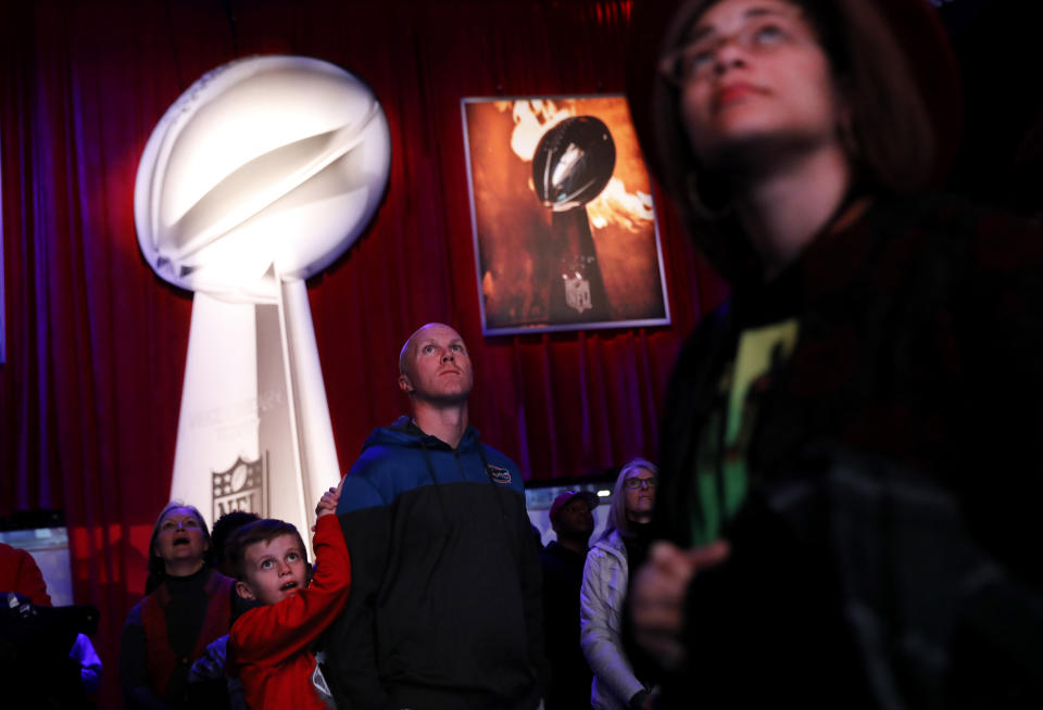 Kyle Williams, right, and his son Grant, 8, of Monroe, Ga., watch a video while waiting in line to see the Vince Lombardi Trophy at the NFL Experience ahead of Sunday's Super Bowl 53 football game between the Los Angeles Rams and New England Patriots in Atlanta, Wednesday, Jan. 30, 2019. (AP Photo/David Goldman)