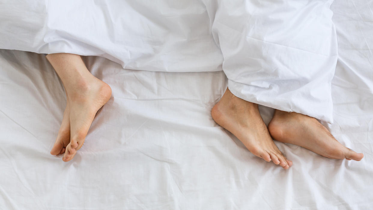 Problems in family relationship. Feet of man and woman in white bed at distance, top view, panorama, free space