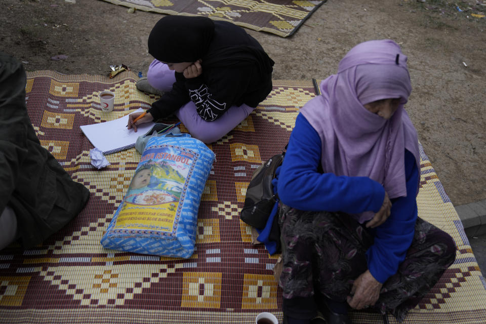 A student does her homework as people rest outside their homes in Duzce, Turkey, Wednesday, Nov. 23, 2022, after a magnitude 5.9 earthquake hit a town in northwest Turkey early Wednesday, causing damage to some buildings and widespread panic. At least 68 people were injured, mostly while trying to flee homes. The earthquake was centered in the town of Golkaya, in Duzce province, some 200 kilometers (125 miles) east of Istanbul, the Disaster and Emergency Management Presidency said.(AP Photo/Khalil Hamra)