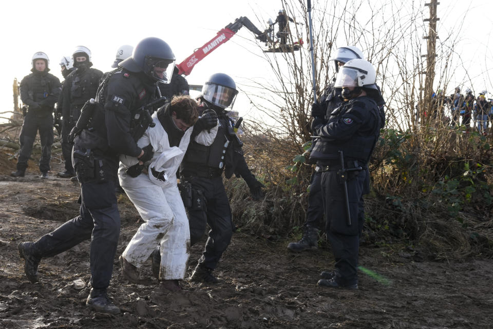 Police officers lead away a demonstrator the at village Luetzerath near Erkelenz, Germany, Tuesday, Jan. 10, 2023. The village of Luetzerath is occupied by climate activists fighting against the demolishing of the village to expand the Garzweiler lignite coal mine near the Dutch border. Poster read: „1,5 degrees celsius means: Luetzerath stays". (AP Photo/Michael Probst)