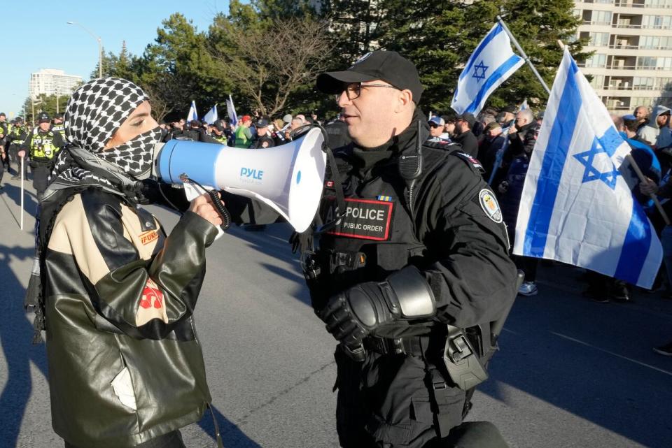 A protester is seen with a police officer at a demonstration outside of a Thornhill, Ont. synagogue on Thursday hosting "the great Israeli Real Estate Event," on Thursday, March 7, 2024. 