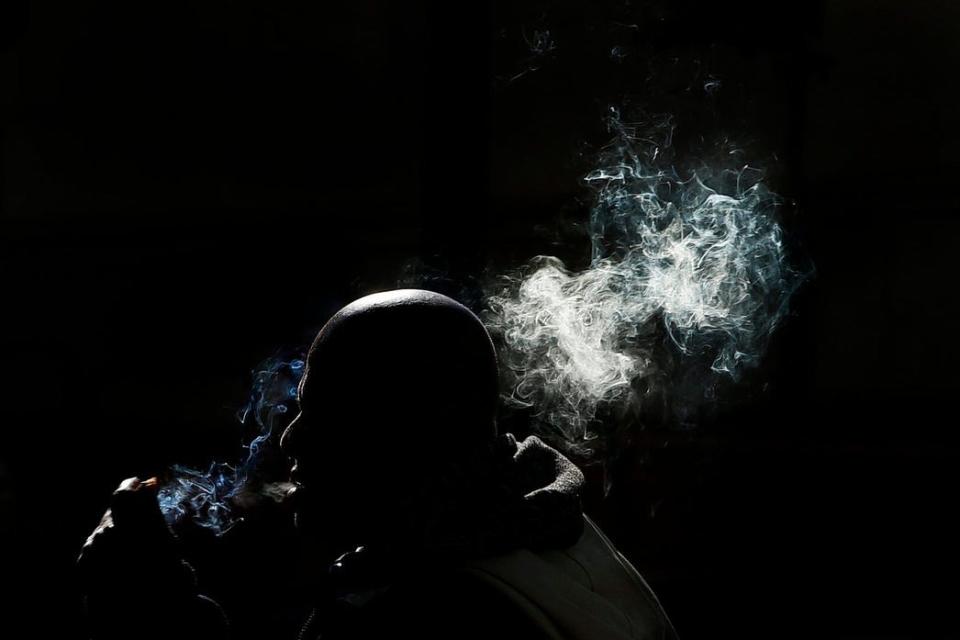 A person is cast in shadows by the buildings around him as he vapes a cigarette on Union Street in New Bedford, Mass.