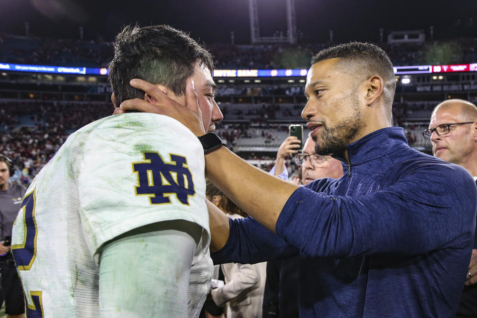 Notre Dame quarterback Tyler Buchner, left, and head coach Marcus Freeman, right, embrace on the field after the Gator Bowl NCAA college football game against South Carolina on Friday, Dec. 30, 2022, in Jacksonville, Fla. (AP Photo/Gary McCullough)