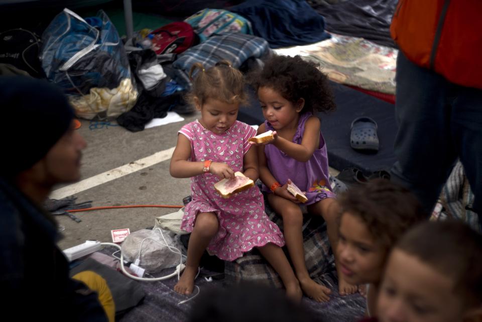 Two girls, part of the migrant caravan, share a sandwich at a shelter in Tijuana, Mexico, Wednesday, Nov. 21, 2018. Migrants camped in Tijuana after traveling in a caravan to reach the U.S are weighing their options after a U.S. court blocked President Donald Trump's asylum ban for illegal border crossers. (AP Photo/Ramon Espinosa)