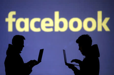 FILE PHOTO: Silhouettes of laptop users are seen next to a screen projection of Facebook logo in this picture illustration taken March 28, 2018. REUTERS/Dado Ruvic/Illustration/File Photo