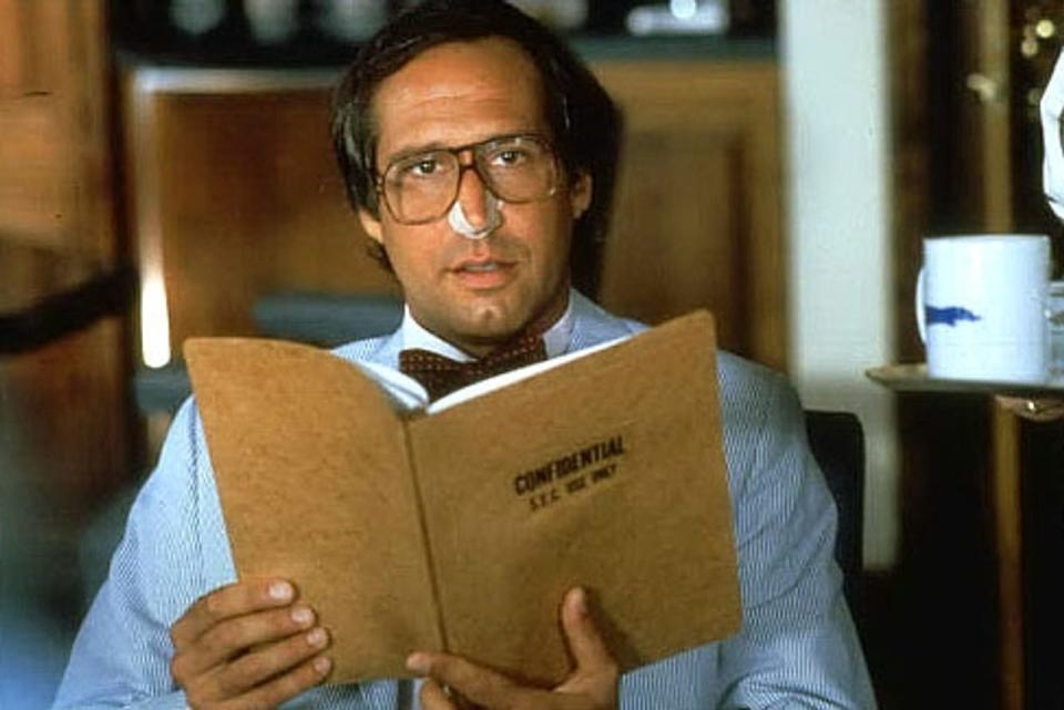 Chevy Chase in glasses holding a folder