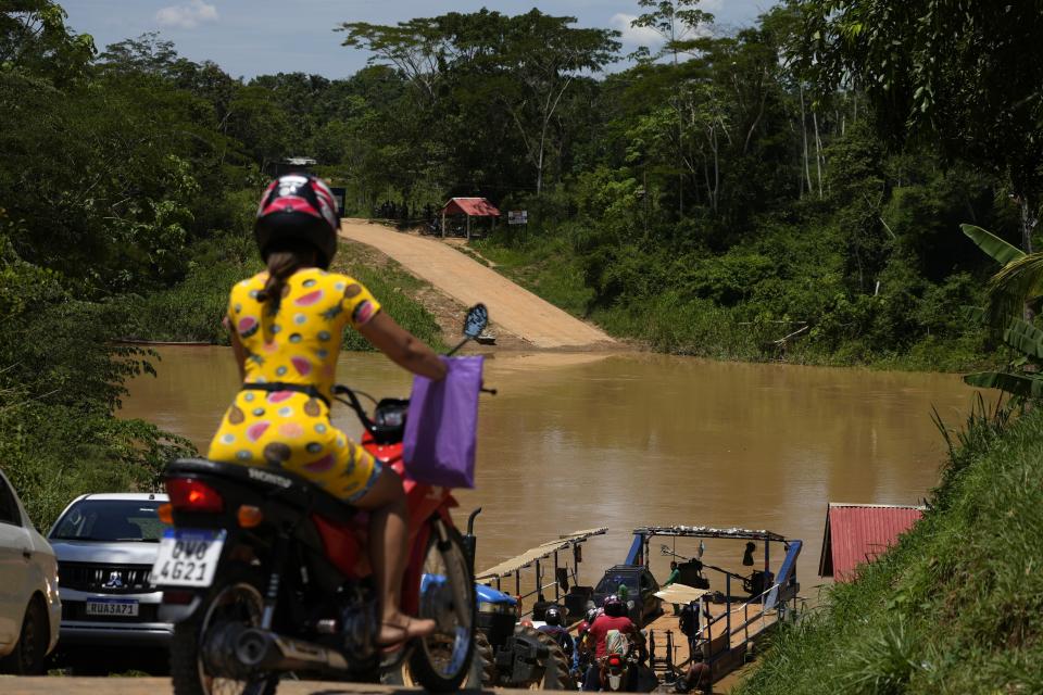 A woman waits on her motorcycle to cross the Acre River on a ferry that connects the city with the rural area of the Chico Mends Extractive Reserve, in the city of Xapuri, Acre state, Brazil, Tuesday, Dec. 6, 2022. The reserve is forest protected in the name of the legendary rubber tapper leader and environmentalist Chico Mendes. (AP Photo/Eraldo Peres)