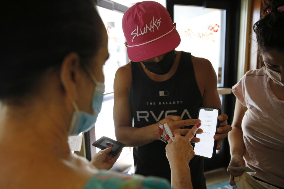 Highway Inn restaurant hostess Ku'uipo Lorenzo, left, checks a COVID-19 test result from Martin Day, center, as his wife, Ashley Day, right, prepares to show her vaccination card on Monday, Oct. 25, 2021, in Honolulu. To comply with local mandates, the restaurant requires all indoor diners to show proof of vaccination or have a recent negative test result before being seated. (AP Photo/Caleb Jones)