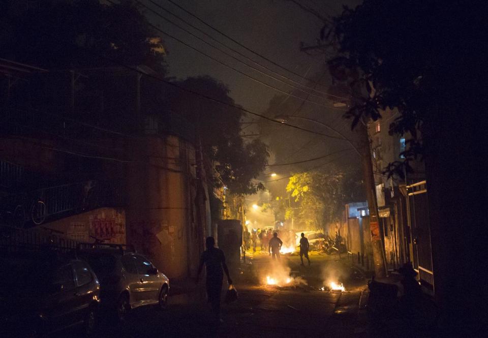 Residents walk among burning barricades during clashes at the Pavao Pavaozinho slum in Rio de Janeiro, Brazil, Tuesday, April 22, 2014. Intense exchanges of gunfire, numerous blazes set alit and a shower of homemade explosives and glass bottles onto a busy avenue in Rio de Janeiro’s main tourist zone erupted Tuesday night after the death of a popular young shantytown resident. (AP Photo/Felipe Dana)