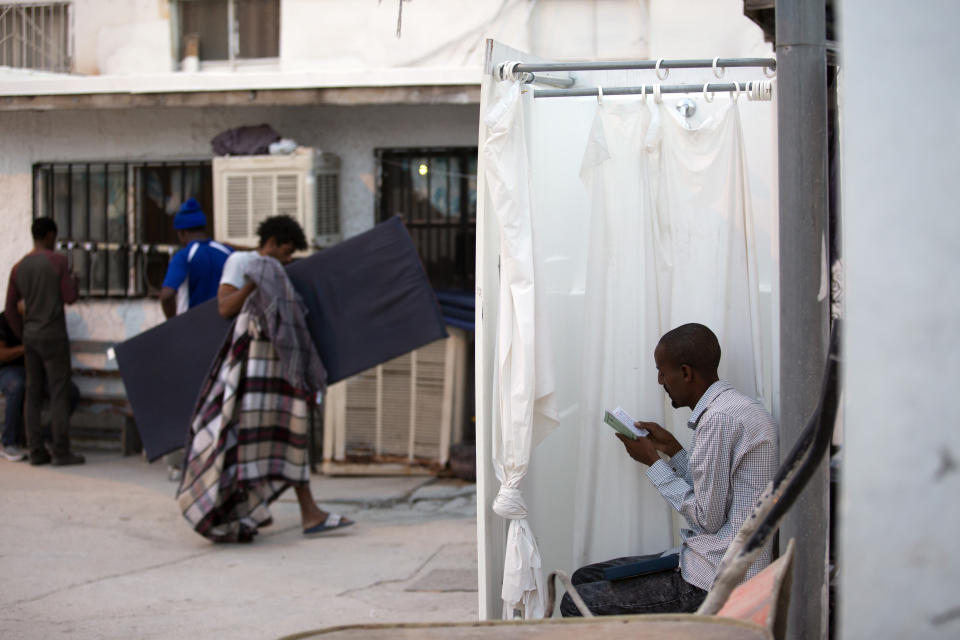 In this July 27, 2019, photo, an Ethiopian man reads his Bible in a shower stall as dawn breaks and others return their mattresses after sleeping outside at El Buen Pastor shelter for migrants in Cuidad Juarez, Mexico. (AP Photo/Gregory Bull)