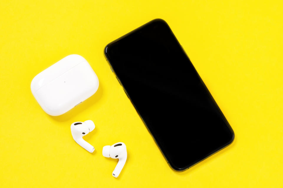 Smartphone Apple iPhone 11 Pro and wireless headphones with charging case on yellow background