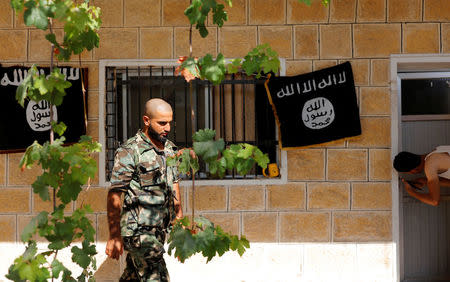 A member of Turkish-backed Free Syrian Army (FSA), seen with the Islamic State flags in the background, walks outside of a building in the border town of Jarablus, Syria, August 31, 2016. REUTERS/Umit Bektas