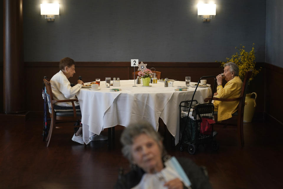 FILE - Ceil Tuder, left, and Olga Rosenson, right, eat together for one of the first times since the start of the pandemic at RiverWalk, an independent senior housing facility, Thursday, April 1, 202, in New York. Since the start of the pandemic, residents had been dining in their rooms. Only recently have they began to use the dining hall again. A focus on the elderly at the start of the nation's vaccination campaign helped protect nursing homes that were ravaged at the height of the U.S. coronavirus outbreak, but they are far from in the clear. New outbreaks, often traced to infected staff members, are still occurring in long-term care centers across the country, causing continued havoc for visitation policies. (AP Photo/Seth Wenig, File)