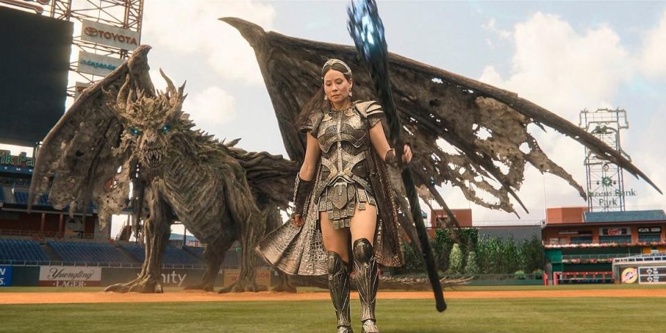 Lucy Liu as a Daughter of Atlas wields the staff of the wizard with a big giant dragon behind her, on the Phillies' field.