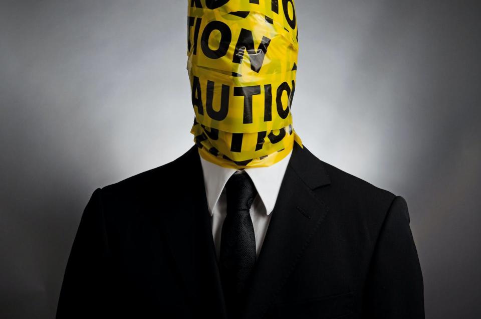 Man in a suit and tie with yellow police tape wrapped around his head and neck.