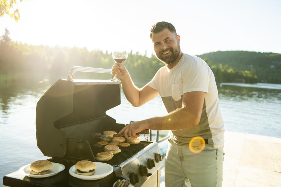 A father family preparing hamburger on a grill outdoors close to a lake