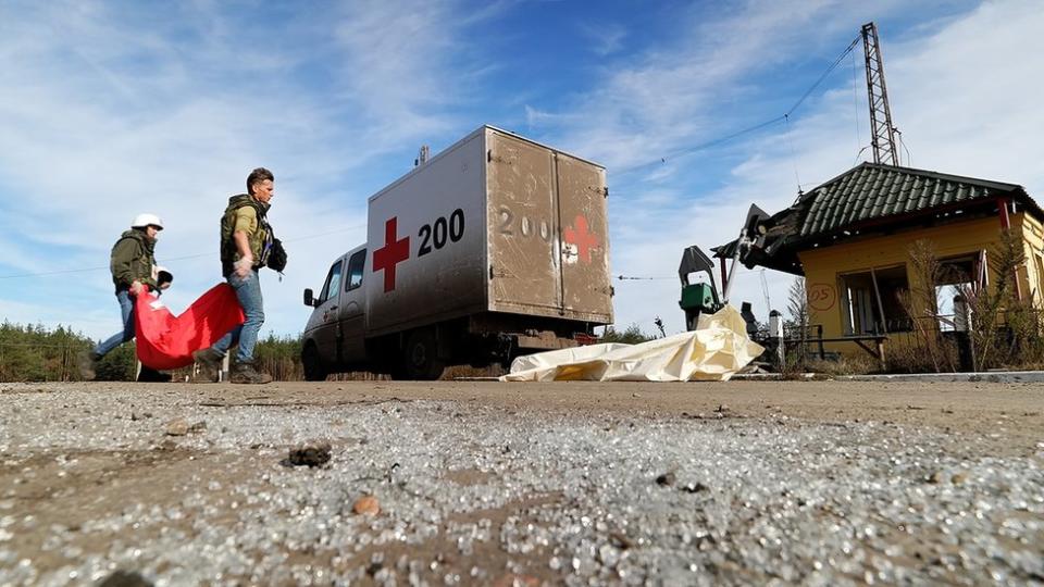 Artur y Denys llevan una bolsa para cadáveres a su camioneta, marcada con una cruz roja y el número 200.