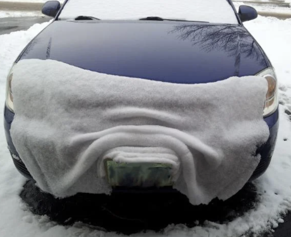 Car covered with snow except the windshield, resembling a mustache