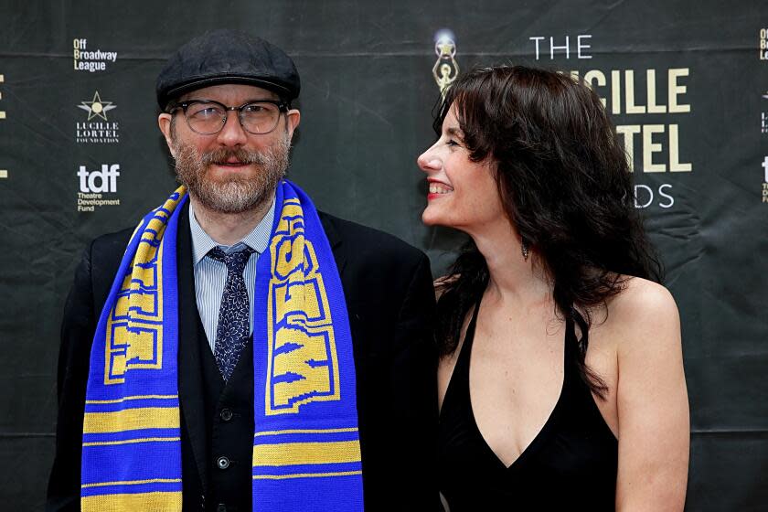 Erik Jensen is wearing a dark suit and hat and smiles as his wife Jessica Blank, in a black dress, smiles at him